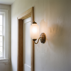 Lisette Milk Glass Wall Sconce in brass, mounted on a plaster hallway wall