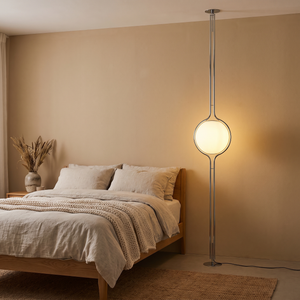Oris floor to ceiling lamp in Silver beside an oak bed with linen bedding, warm evening glow