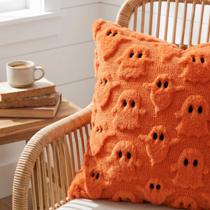 Pumpkin Ghost plush cushion close up on a rattan chair in a reading nook